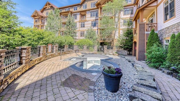Un edificio de varios pisos con fachada de piedra, un patio central con jacuzzi y un camino de piedra.