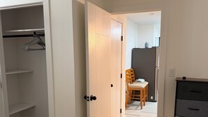 A bedroom with a closet, a dresser, and a dining area in the background. - Brand new basement suite with private entrance, 3-5 minutes to market and parks (Saskatoon)