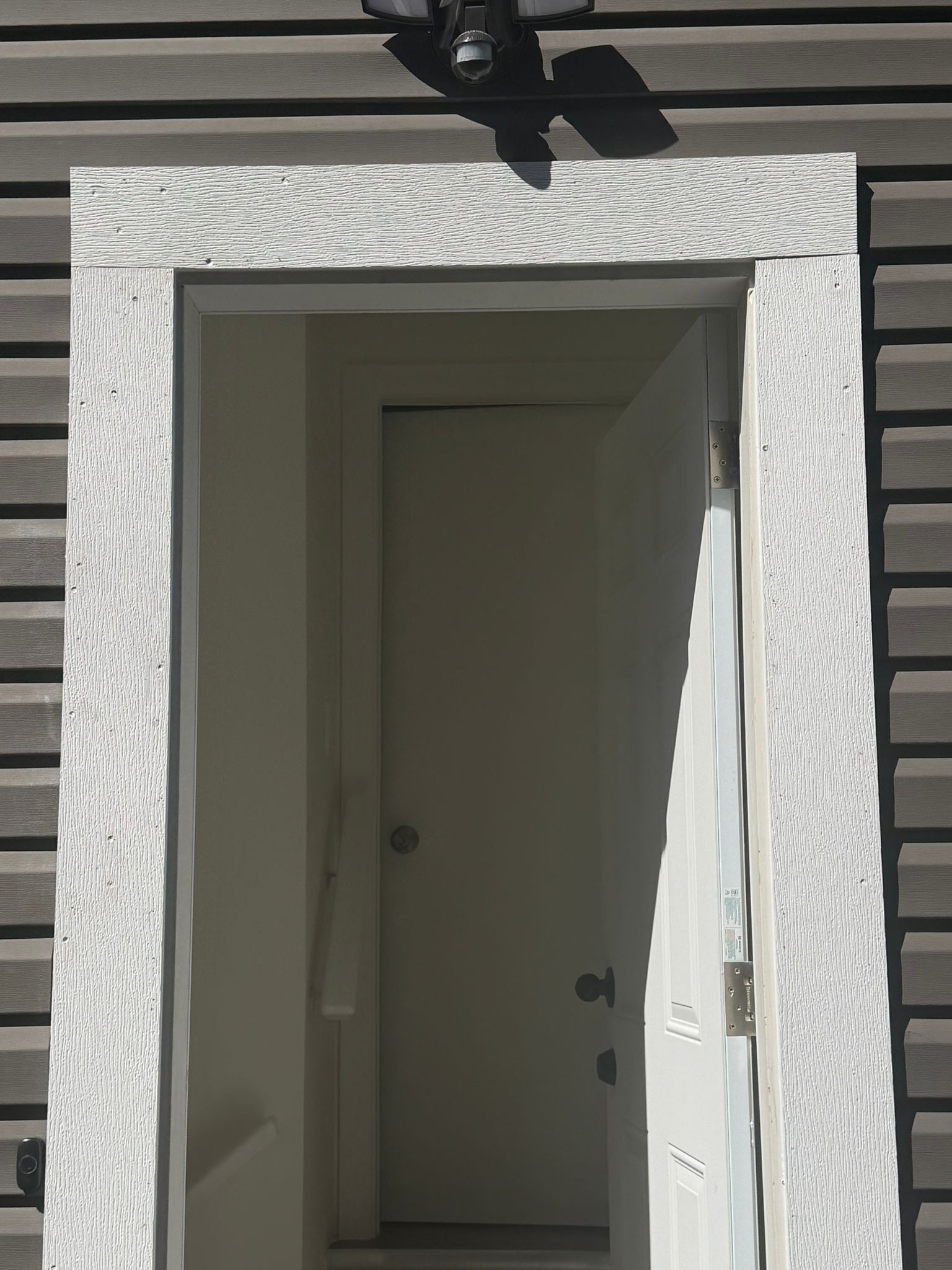 Een deur met een witte omlijsting, een plafondventilator erboven en een grijze buitenmuur.