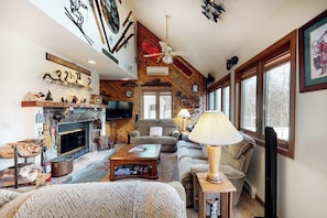 A cozy living room with a fireplace, a television, and a large window. - Comfortable Townhome with Shared Pool, Private Hot Tub & Wood-Burning Fireplace (Stratton)