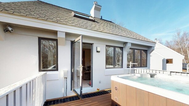 Een modern huis met een houten terras, een jacuzzi en een schuifdeur naar de binnenruimte.