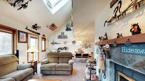 Een gezellige woonkamer met een open haard, een bank, een salontafel en een eethoek op de achtergrond.