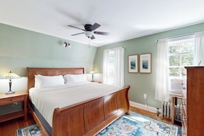 A bedroom with a wooden bed, a ceiling fan, a window with curtains, and a radiator. - Classic village home with large porch, washer/dryer, cable, grill & partial AC (Manchester)