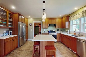 Cucina con mobili in legno, isola centrale, elettrodomestici in acciaio inossidabile e lampadario.