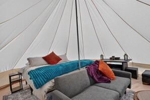 A tent with a bed, a grey sofa, and a small table with lanterns. - Glamp Palazzo at Camp Little Lemhi (Swan Valley)