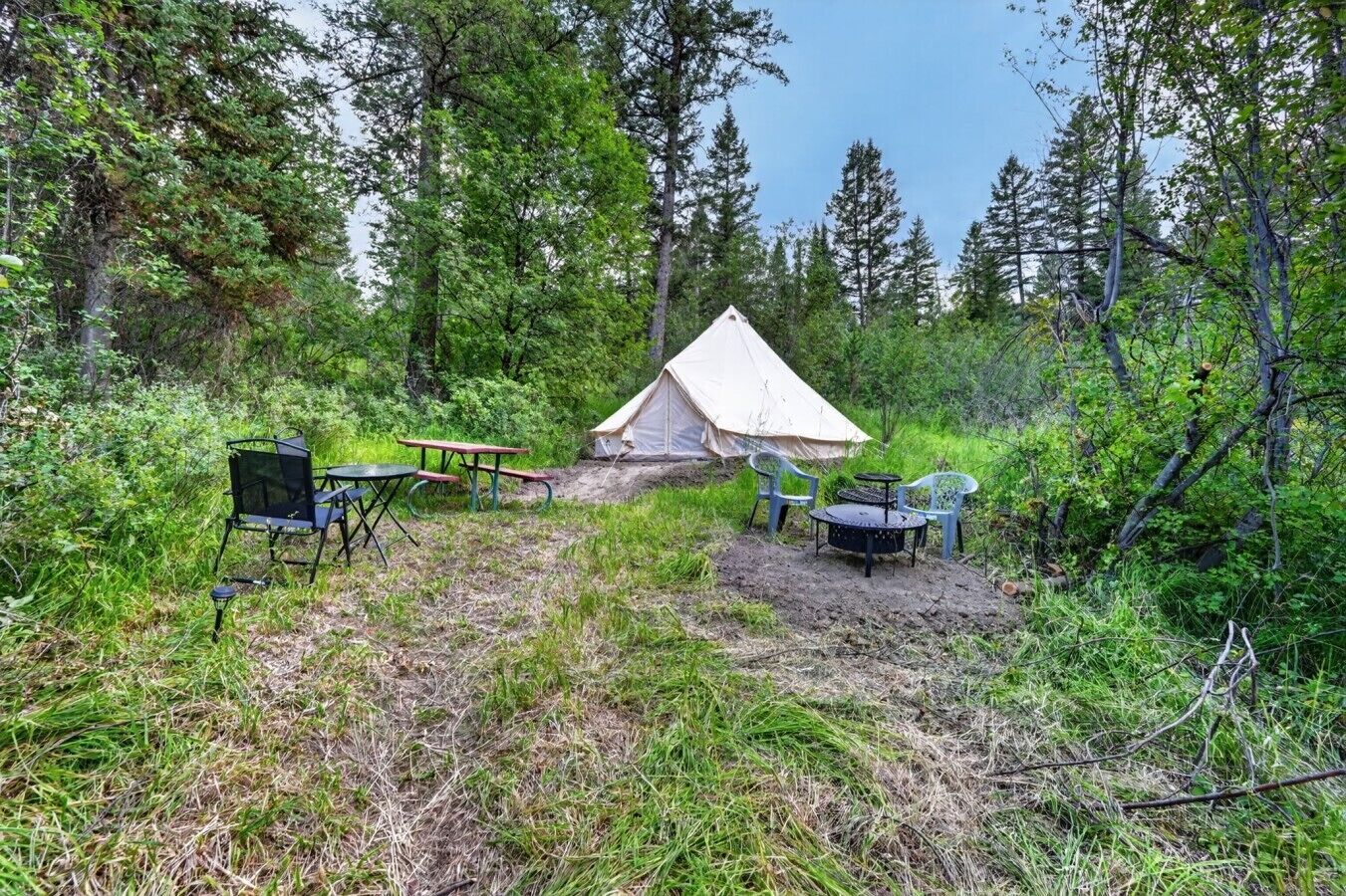 A tent with a picnic table and chairs in a forested area.
