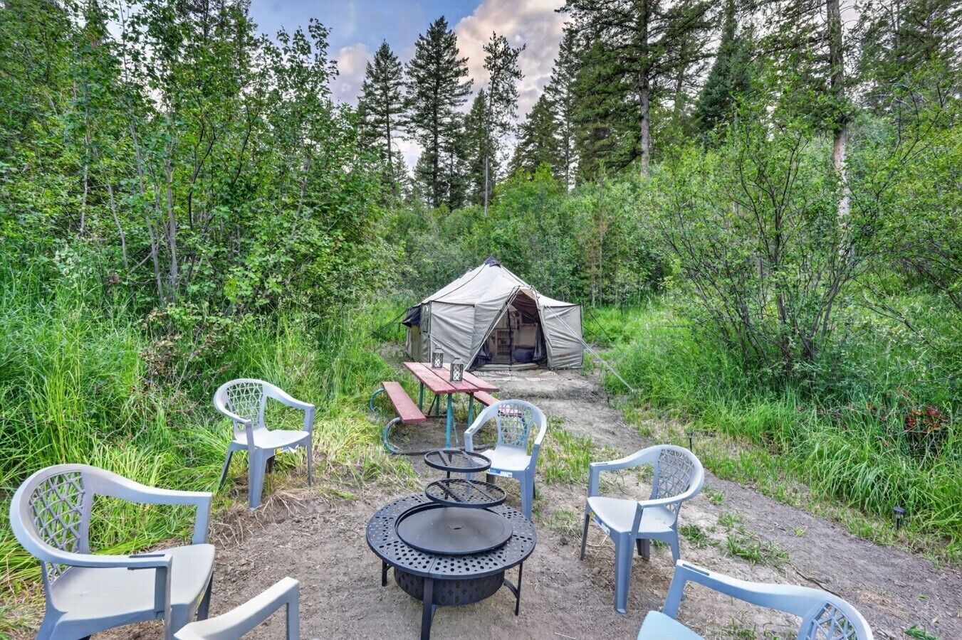 Een camping met een tent, picknicktafel en stoelen.