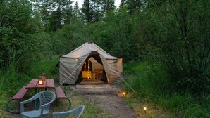 Een tent met een geopende ingang, een tafel met stoelen en een lantaarn erbuiten.
