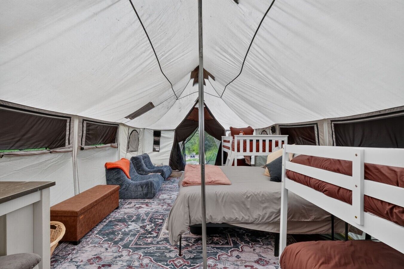 A tent with a bed, two sofas, a table, and a bench.