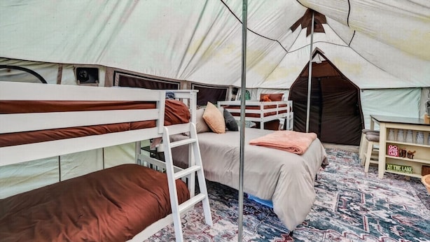 Een tent met stapelbedden, een ladder, een tafeltje en een plank met spullen.