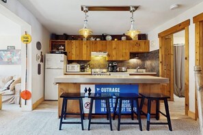 Eine kompakte Küche mit Holzausbau, einer zentralen Kochinsel und hängenden Pendelleuchten.