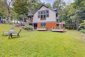 Ein zweistöckiges Haus mit Terrasse, umgeben von einem gepflegten Rasen und Bäumen.