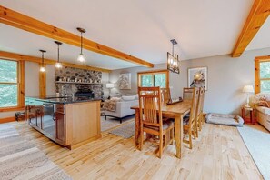 Eine geräumige Küche mit Holzbalken, ein Essbereich mit Tisch und Stühlen sowie ein gemütliches Wohnzimmer mit Sofa und Kamin.