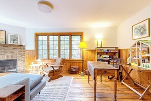 Una sala de estar acogedora con chimenea, muebles de madera, una mesa de centro, una estantería y una ventana con vistas a árboles.