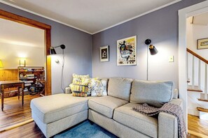 Una sala de estar con un sofá modular, una mesa de madera con libros y una escalera.