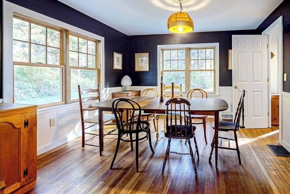 Comedor con mesa y sillas de madera, ventanas amplias y una lámpara colgante.
