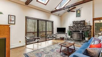 A spacious living room with a fireplace, large windows, and a ceiling fan.