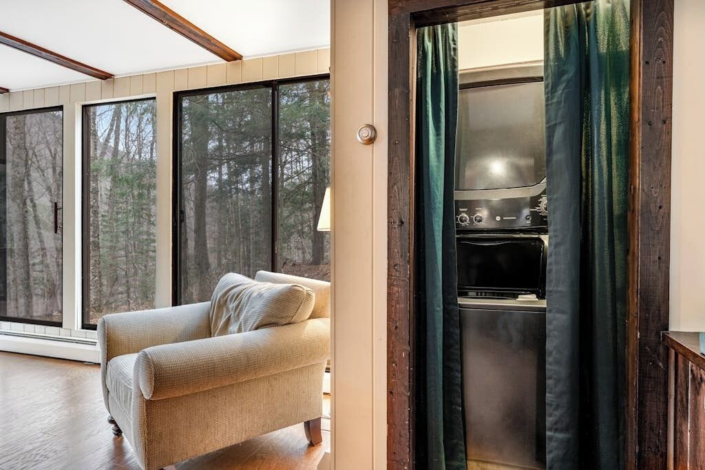 Een gezellige woonkamer met een bank, een groot raam en uitzicht op bomen.