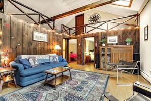 A cozy living room with a blue sofa, wooden walls, a patterned rug, and a bookshelf. - Dog-friendly cabin with forest setting, woodstove & deck - near Killington (Plymouth)