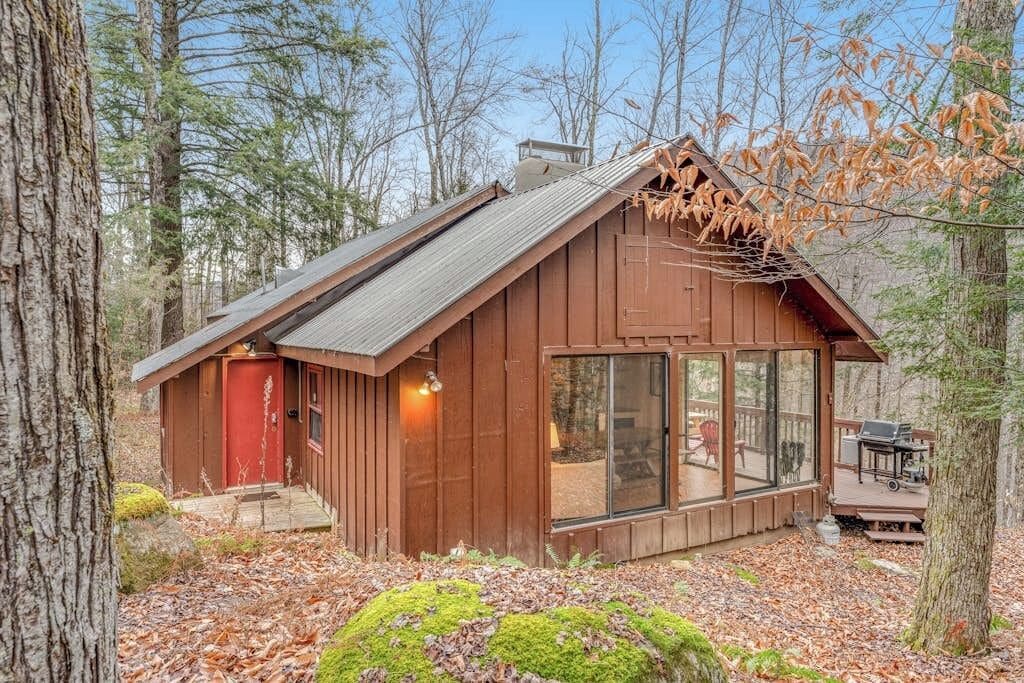 Une cabane avec une porte rouge, de grandes fenêtres et une terrasse.