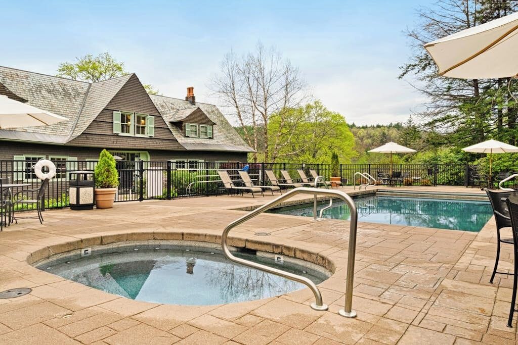 A pool area with lounge chairs, a hot tub, and a building with a sloped roof.