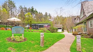 A sign for Castle Hill Spa, a pathway leading to a building, and a stone pillar. - Two-story townhome with forest/mountain view, gas fireplace, pool, gym & saunas (Proctorsville)