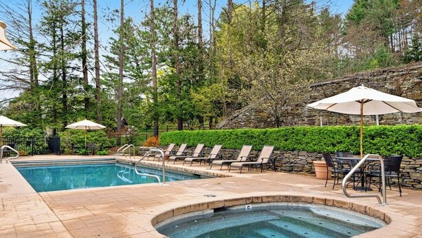 A swimming pool with lounge chairs and umbrellas, surrounded by trees and stone walls. - Two-story townhome with forest/mountain view, gas fireplace, pool, gym & saunas (Proctorsville)