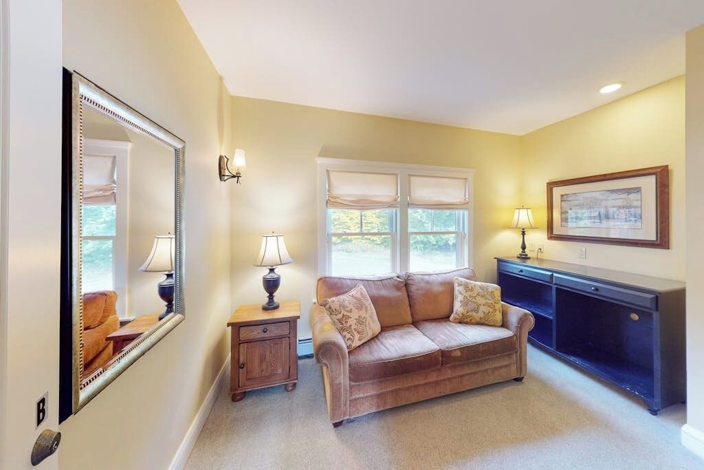 A living room with a sofa, a mirror, a lamp, a window, and a framed picture on the wall.