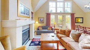 A living room with a fireplace, a sofa, a coffee table, and a large window. - Two-story townhome with forest/mountain view, gas fireplace, pool, gym & saunas (Proctorsville)