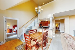 Amplia sala de estar con una mesa de comedor de madera, una escalera y una cocina al fondo.