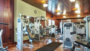 A gym with various exercise machines, wooden walls, and a black mat on the floor. - Two-story townhome with forest/mountain view, gas fireplace, pool, gym & saunas (Proctorsville)