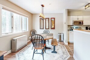 A modern kitchen with a dining area, large windows, and a central island. - Mountain-view condo with private balcony, fireplace, & updated interior (Stratton)