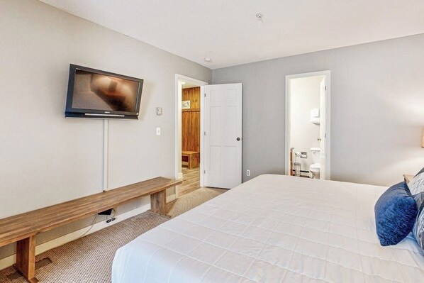 A bedroom with a bed, a bench, a television, and two doors leading to other rooms. - Remodeled Vantage Point condo with wood fireplace, walk to the village (Stratton)