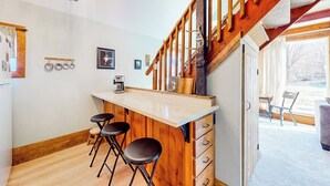 Eine Küche mit einer Holzinsel, Barhocker, einer Kaffeemaschine und einer Treppe, die auf einen Balkon führt.