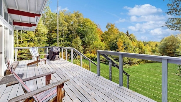 Un terrazzino in legno con ringhiera, una sedia e un barbecue.