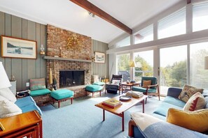 A cozy living room with a fireplace, comfortable seating, and large windows. - Picturesque, Euro-style ski chalet with beautiful setting, deck & fireplace (Peru)