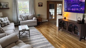 A living room with a sofa, a coffee table, a TV, and a wooden floor. -  3-bedroom house in tranquil Millinocket (Millinocket)