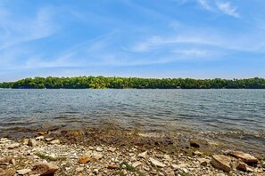 Ein See mit steiniger Uferlinie und einer bewaldeten Insel im Hintergrund.