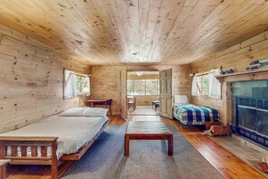 Eine Holzhütte mit Bett, Bank, Kamin und Blick durch eine offene Tür.