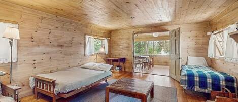 A wooden cabin with two beds, a dining table, and a view through a large window.