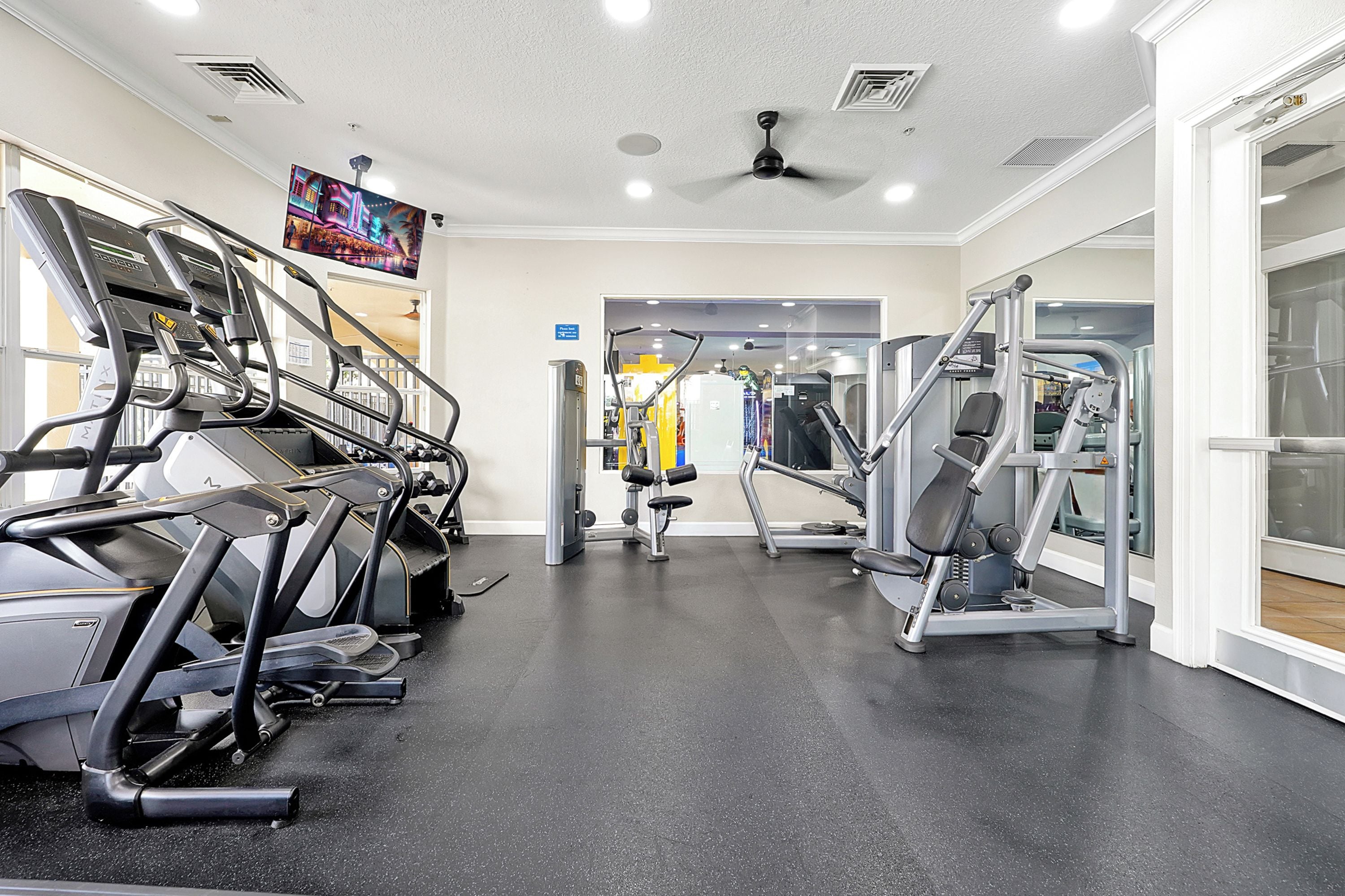 A gym with treadmills, weight machines, and a television screen.