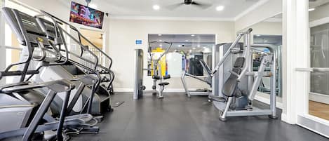 A gym with treadmills, weight machines, and a television screen.