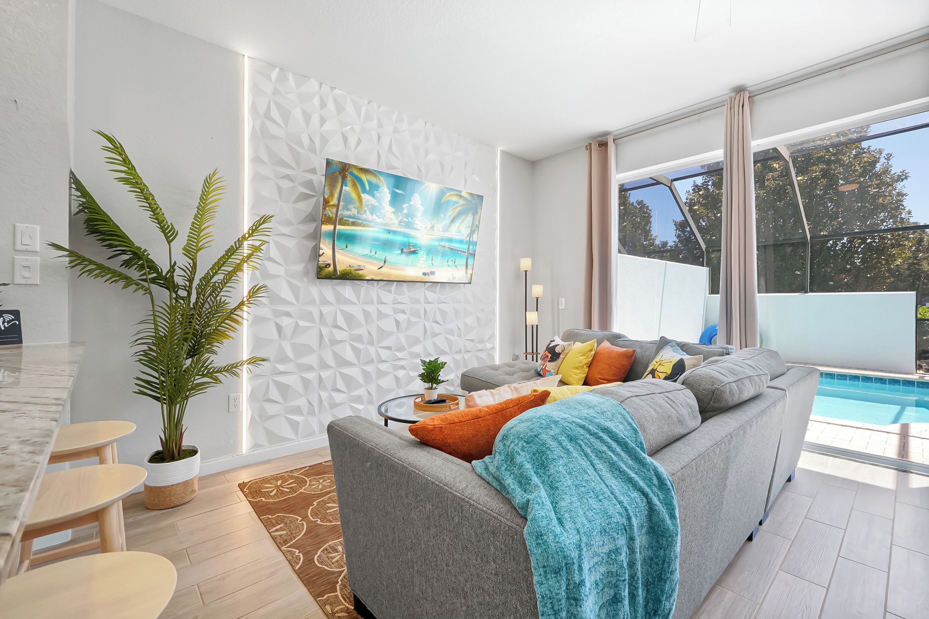 A modern living room with a grey sofa, a large painting of a beach, a dining area with a marble table, and a view of a swimming pool.