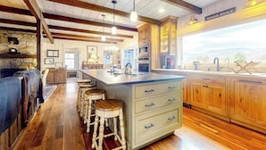 A kitchen with wooden cabinets, a central island with stools, and a view of the outdoors.