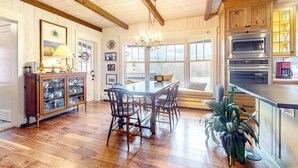 A wooden-paneled room with a dining table, chairs, a chandelier, and a kitchen with a microwave and oven.
