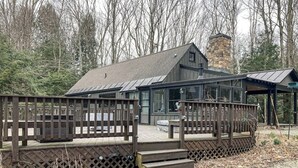 A cabin with a wooden deck, a stone chimney, and a glass enclosure.