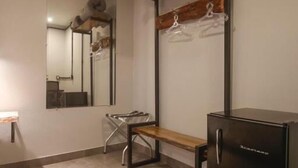 Quarto com um banco de madeira, um armário preto, um espelho e um cabideiro.