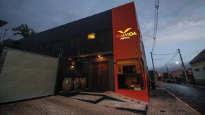 Um hotel moderno com fachada destacada em vermelho e preto, entrada visível e rua pavimentada ao fundo.