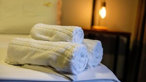 Uma cama com toalhas brancas bem dobradas e uma luminária de cabeceira.