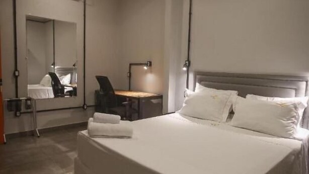 Quarto de hotel com cama grande, escrivaninha, cadeira, espelho e ar condicionado fixado na parede.
